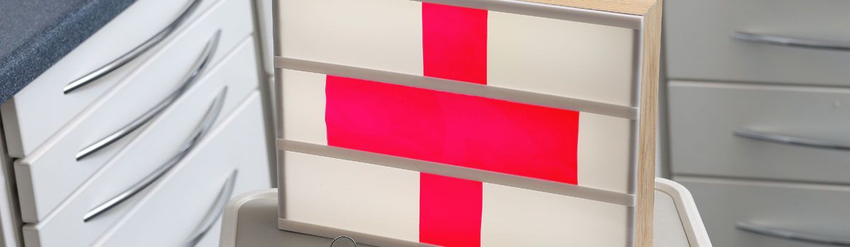 Emergency red cross symbol on illuminated board in dental treatment room